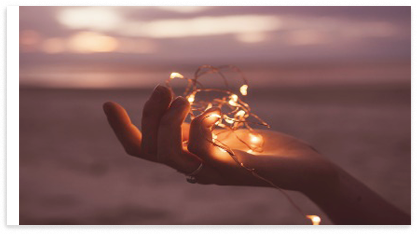 Eine Hand hält eine Lichterkette am Strand