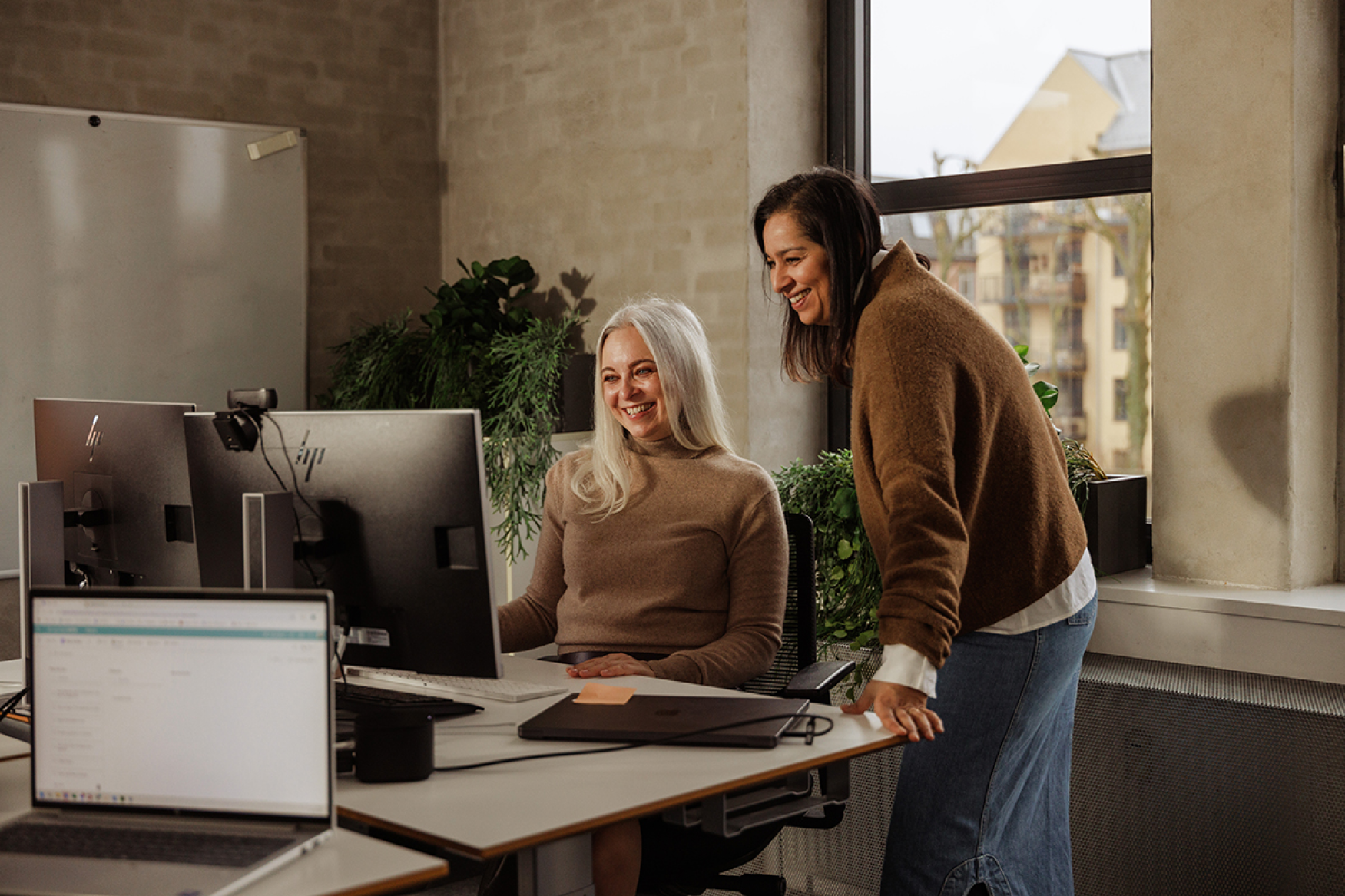 Manager assisting an employee at her desk while they look at the computer screen together.
