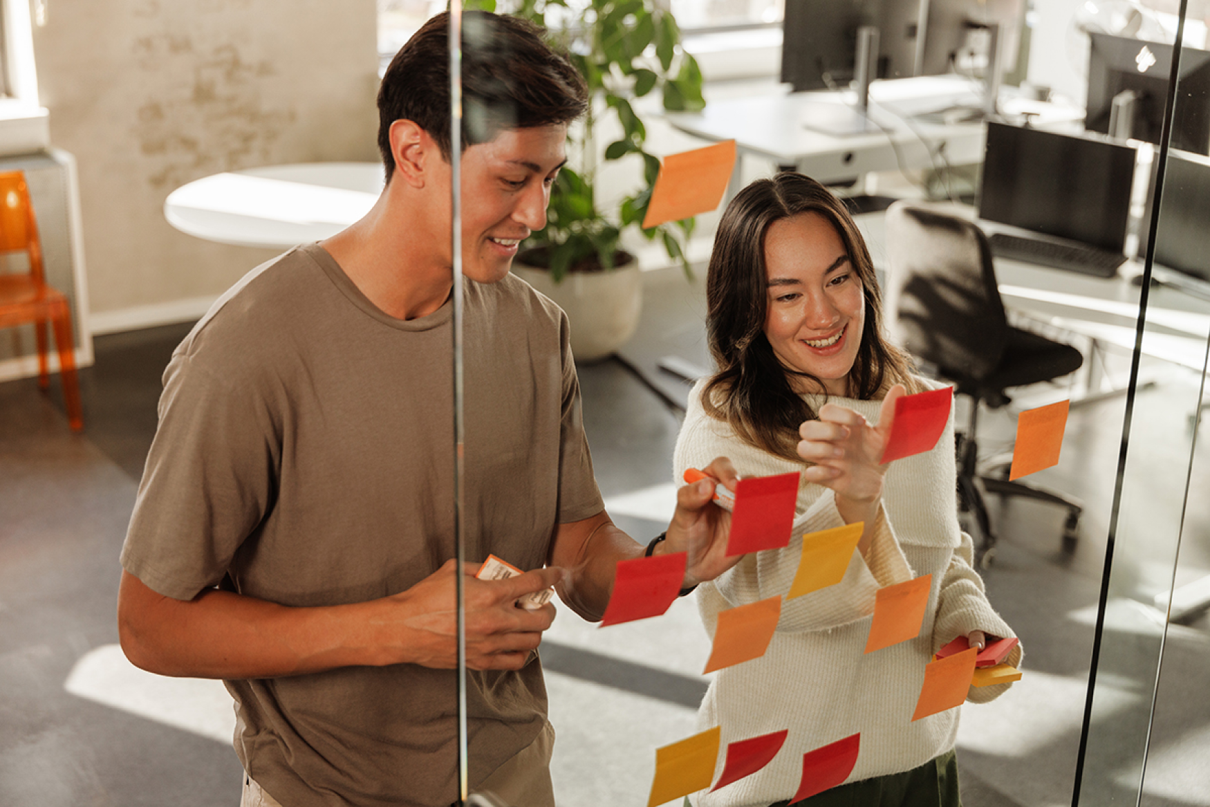 Male and female coworkers brainstorming by placing sticky notes on glass