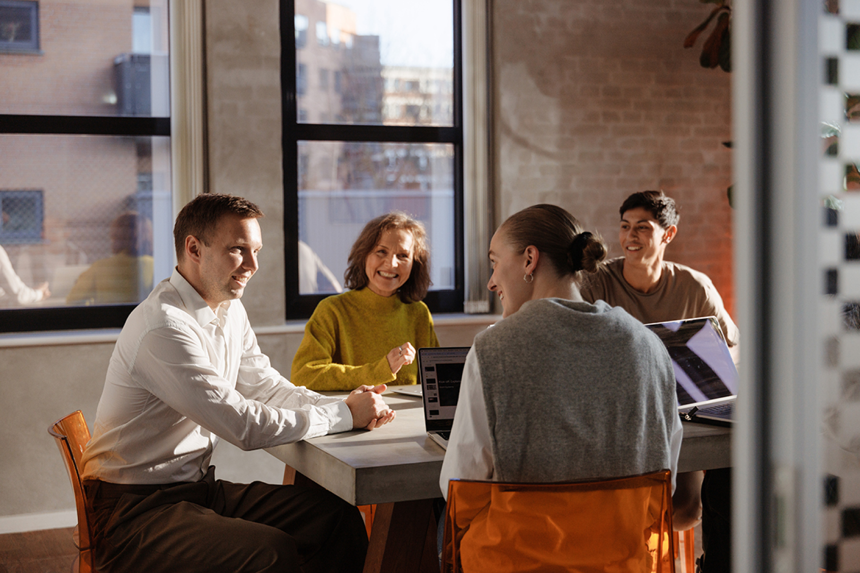 A team of four people sitting at a table and smiling while collaborating in a meeting