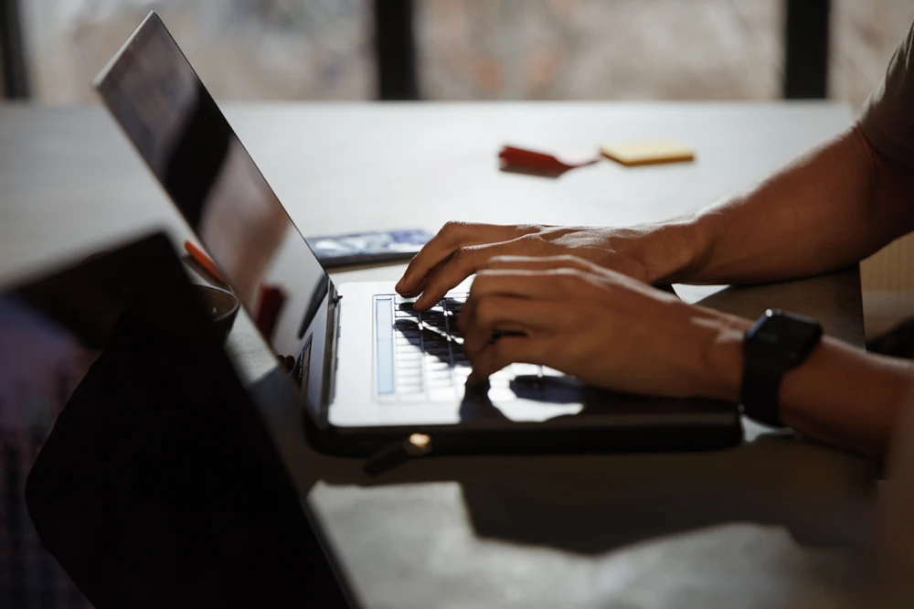 Man's hands typing on laptop at desk next to office supplies