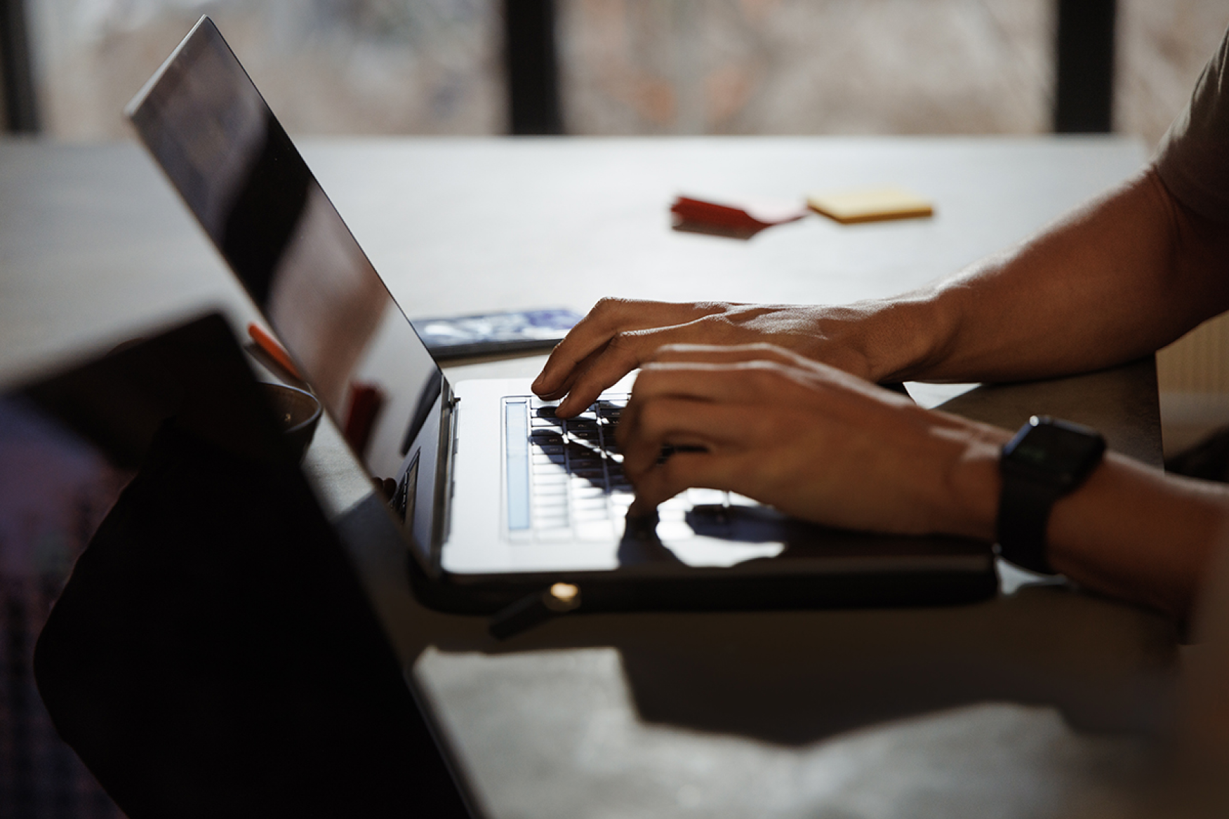 Man's hands typing on laptop at desk next to office supplies