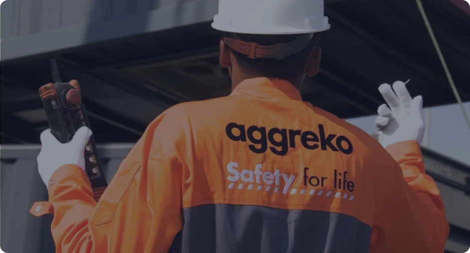 An Aggreko employee wearing an orange safety jacket working on equipment at a construction site